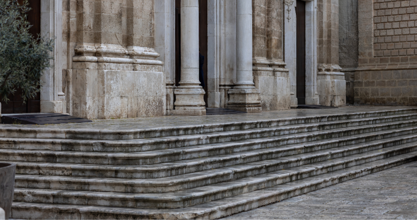 Historic stone stairs leading up to the grand entrance of an ancient european church or building with classical columns and weathered marble texture