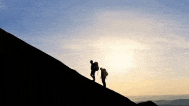 Silhouettes of a man and a woman with backpacks climbing to the top of the mountain