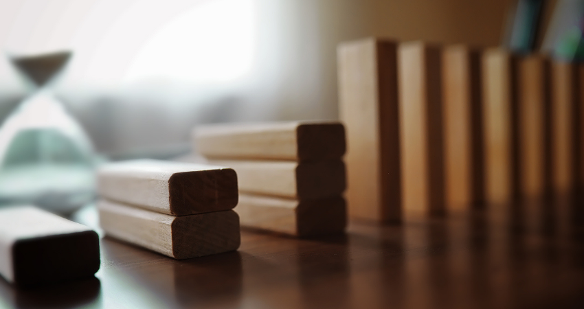 Domino effect concept with wooden tiles blocked by hourglass with background